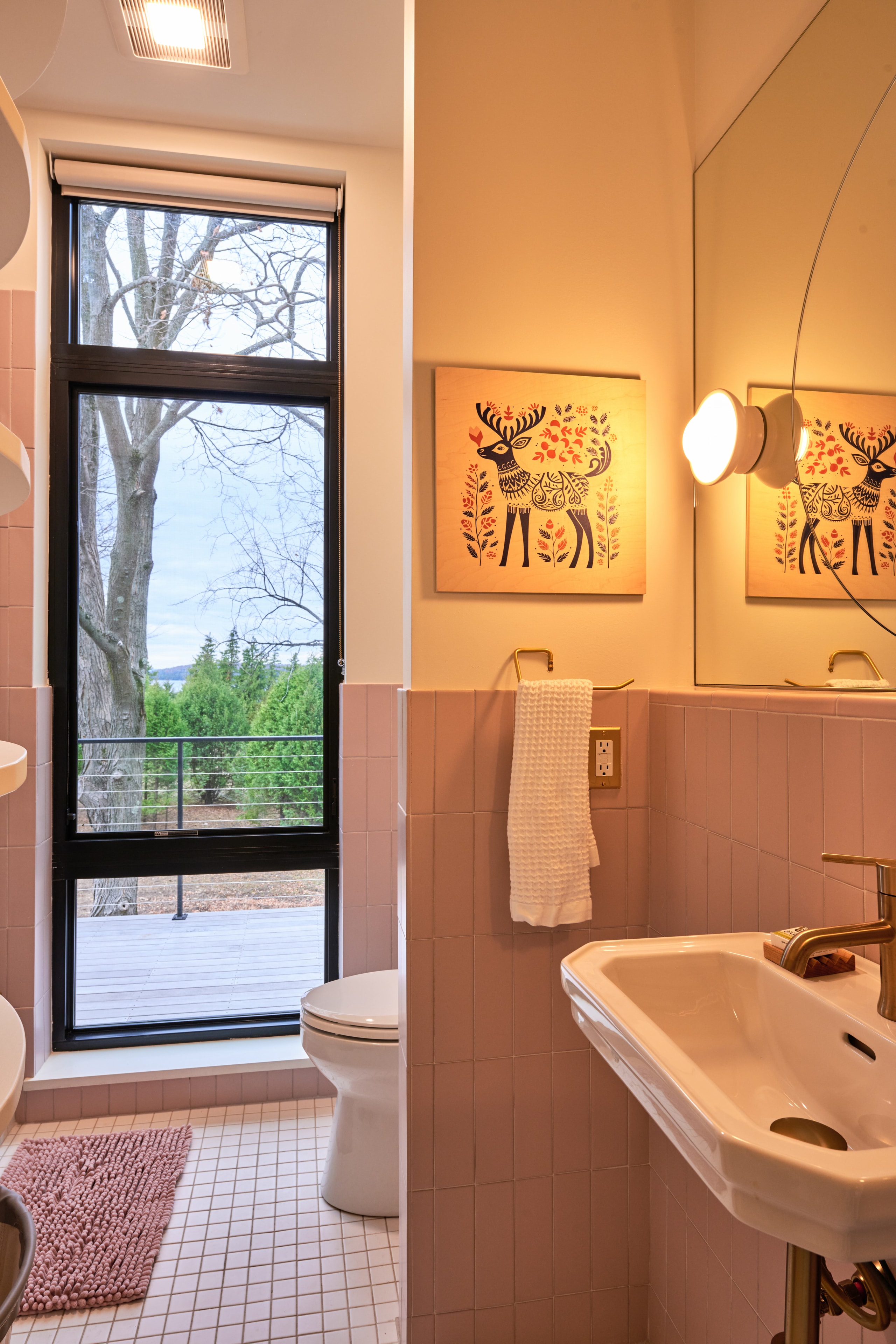 Bathroom with vintage pink tile, brass fixtures, and a tall window framing lake and tree views