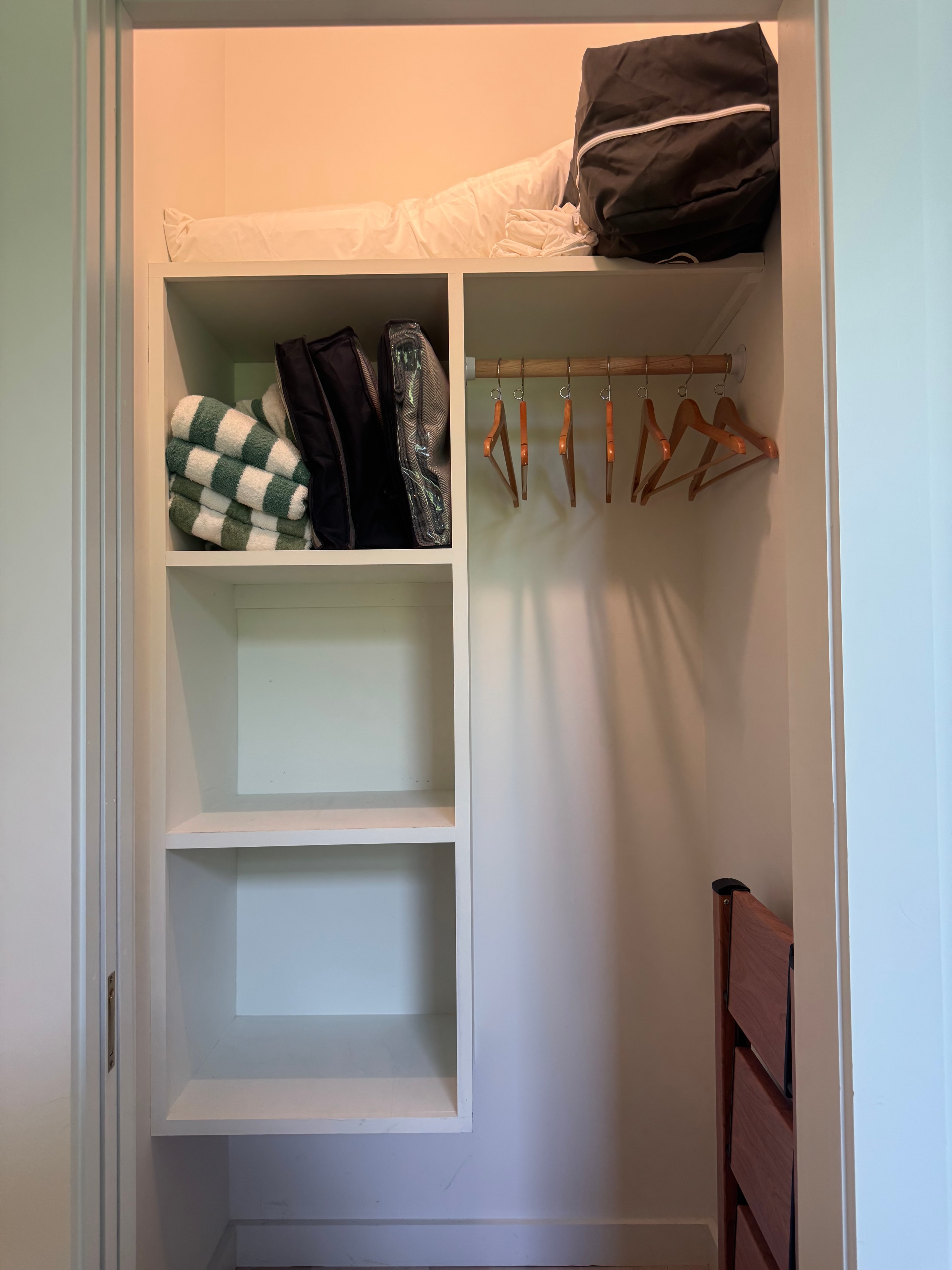 Built-in closet with open shelving, wooden hangers, extra blankets, and striped wool socks