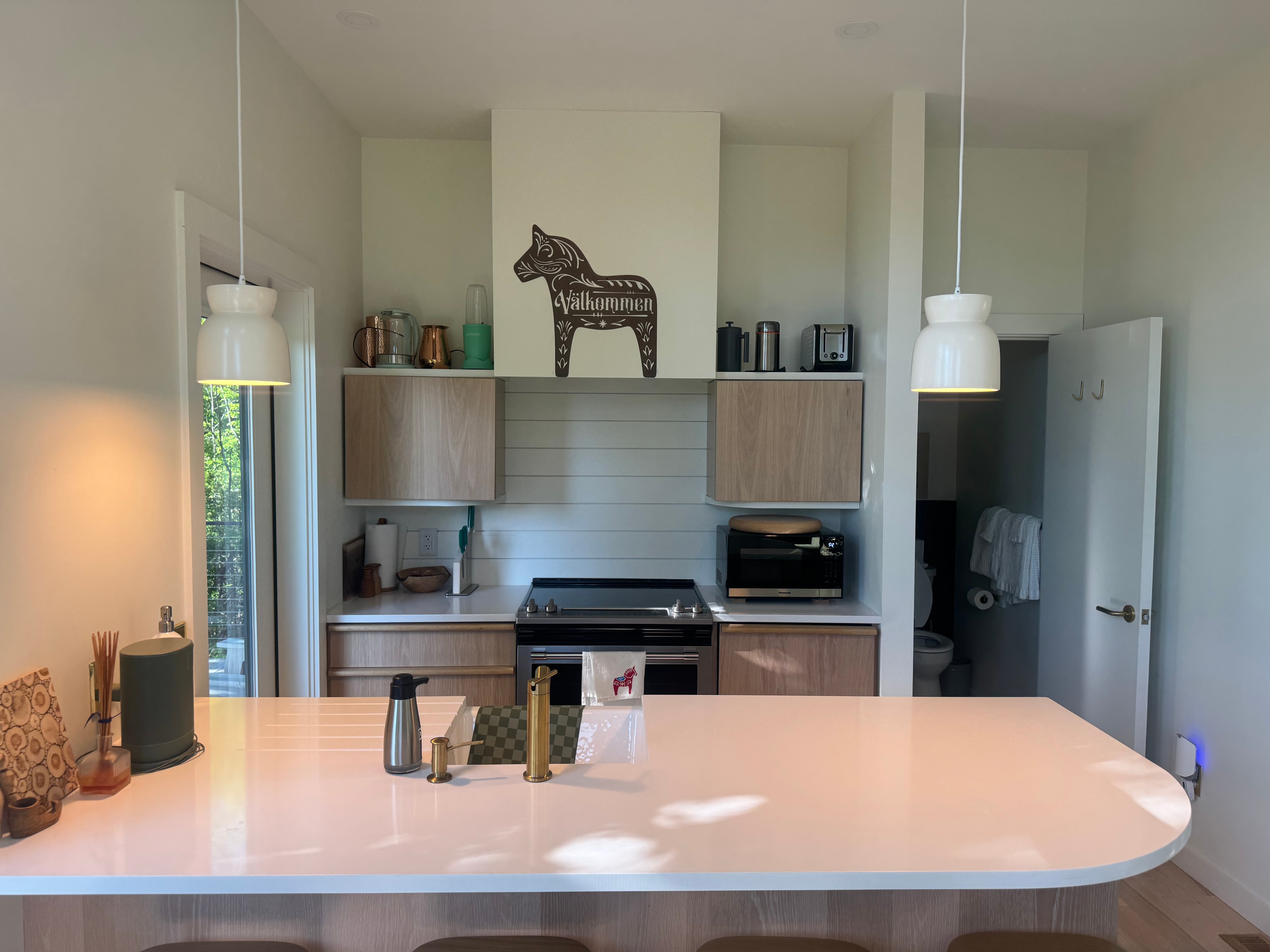 Kitchen with Scandinavian oak cabinetry, quartz island, pendant lights, and a Välkommen Dala horse above the range