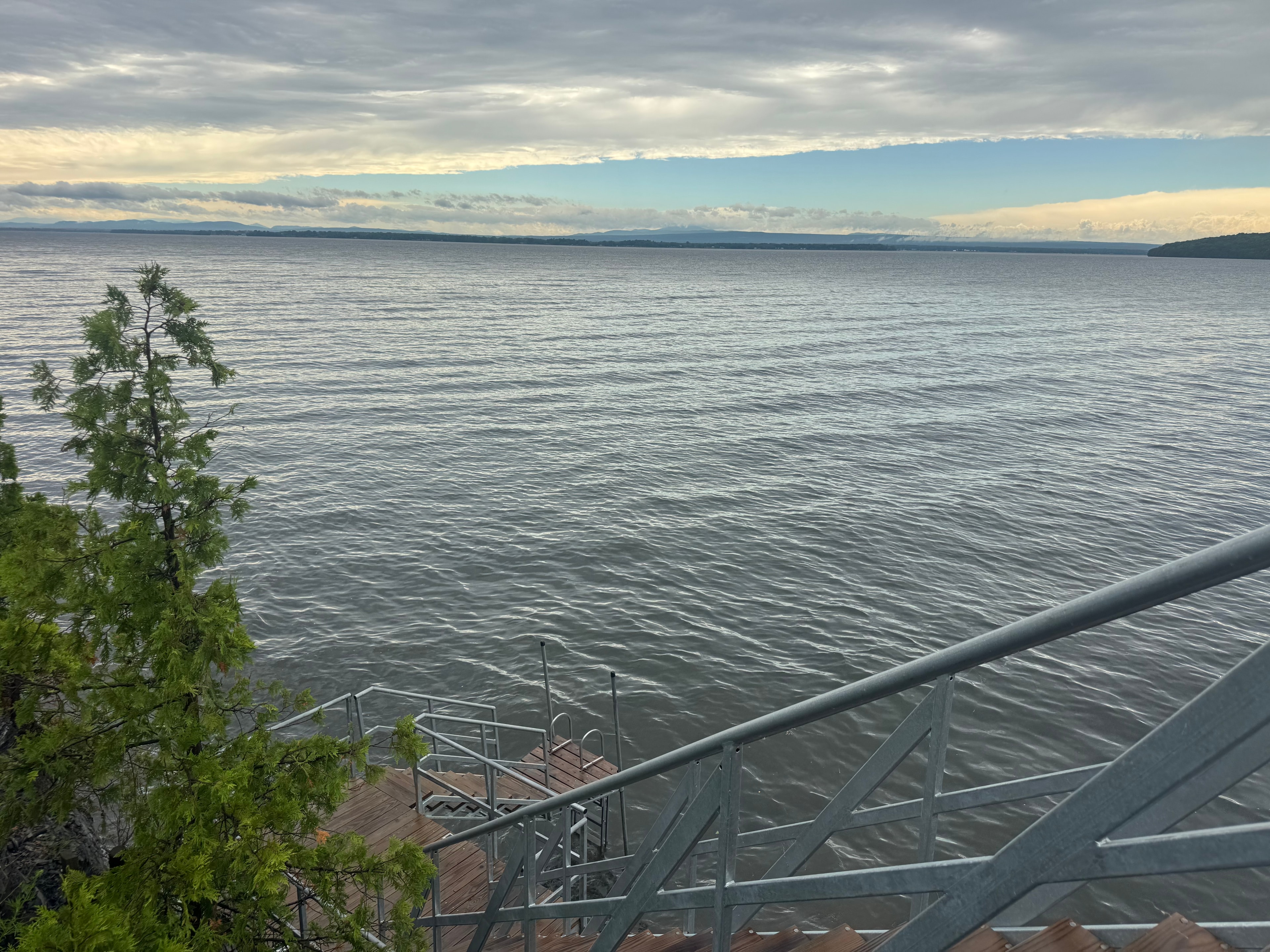 View from the dock over Lake Champlain — calm water, a wooden pier, and the Adirondacks in the distance
